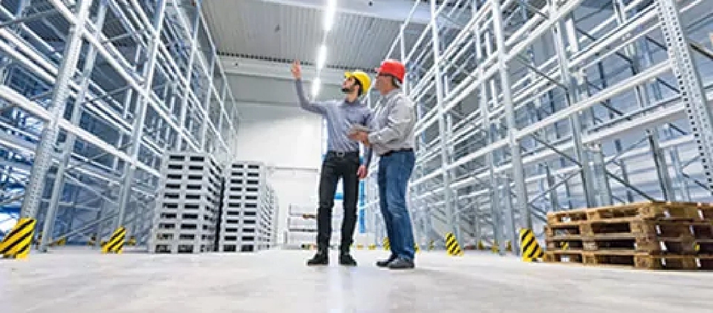 Two men in hard hats stand in a warehouse.