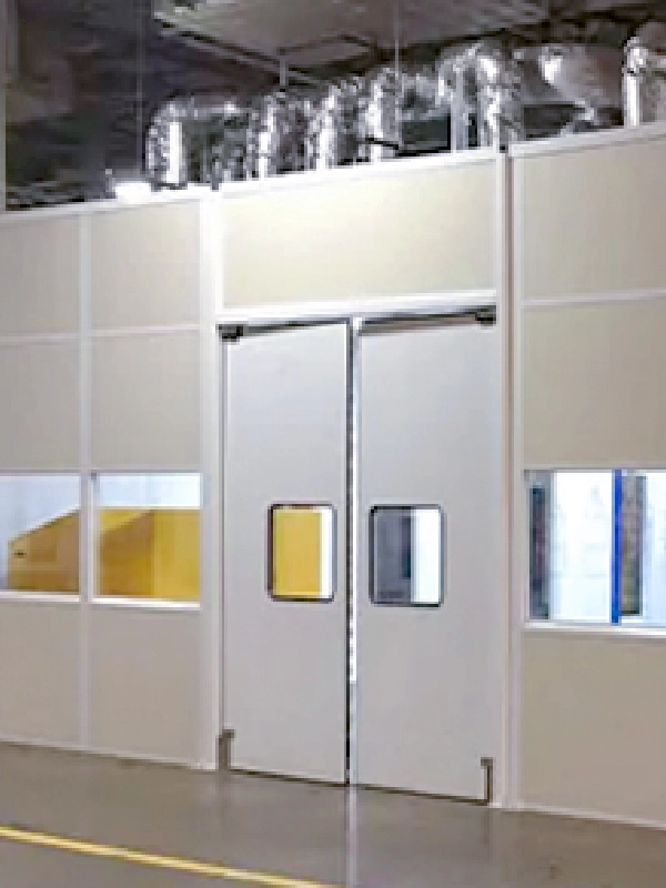 A cleanroom with double swing doors and windows on both sides, located inside an industrial facility with exposed ductwork above, showcases the versatility of modular buildings.
