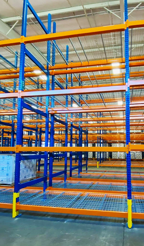 Rows of tall, empty Warehouse Storage Rack Systems with blue frames and orange beams stand inside a warehouse with concrete floors and a high ceiling.