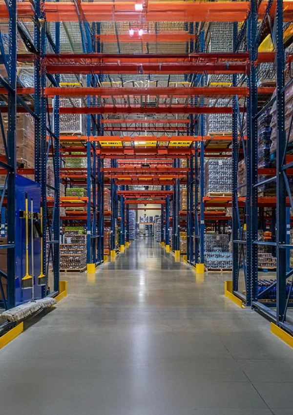 Large warehouse interior featuring tall Warehouse Storage Rack Systems, stacked pallets, and wide clear aisle under bright overhead lighting.