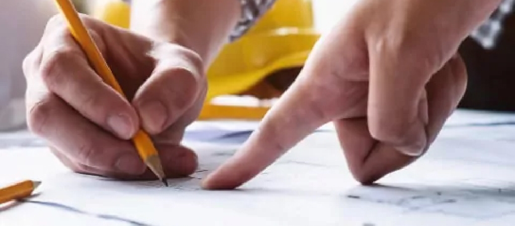 Close-up of two hands reviewing and marking a blueprint with a pencil; one hand is pointing at a specific spot related to Turnkey Warehouse Projects.