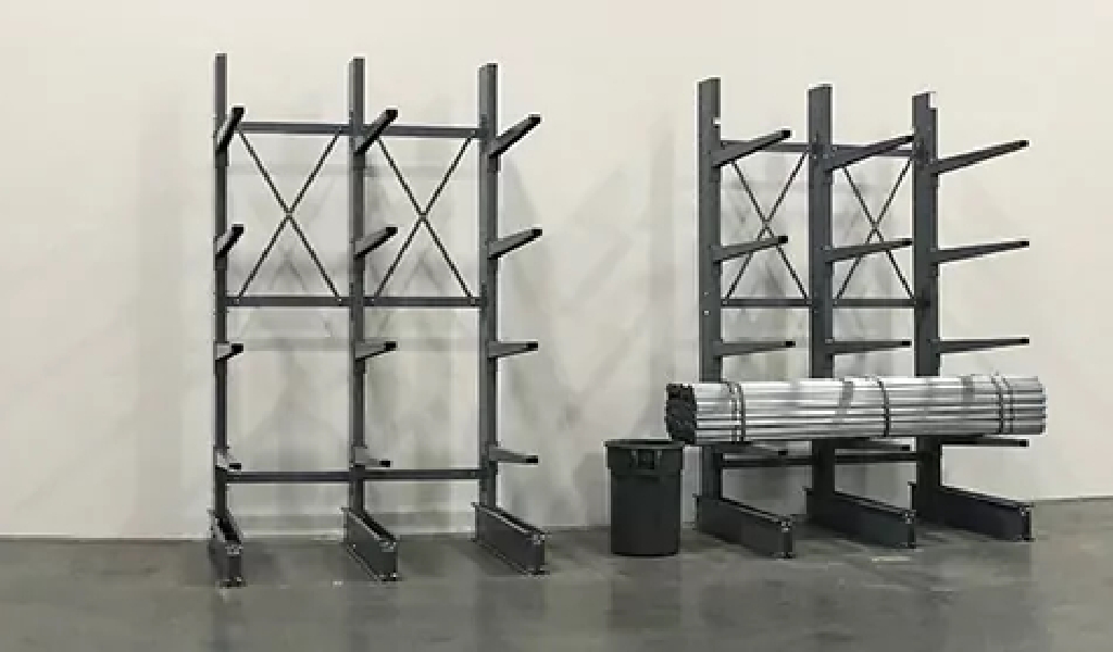 Two empty metal storage racks, including a cantilever rack, stand against a plain wall. A trash bin sits nearby, and one rack holds bundled metal pipes.