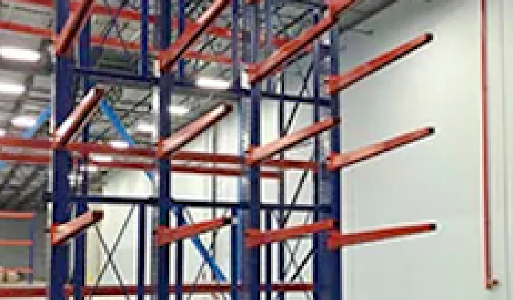 Industrial Cantilever Rack shelving featuring multiple empty red horizontal arms and blue vertical supports stands inside a large, well-lit facility.