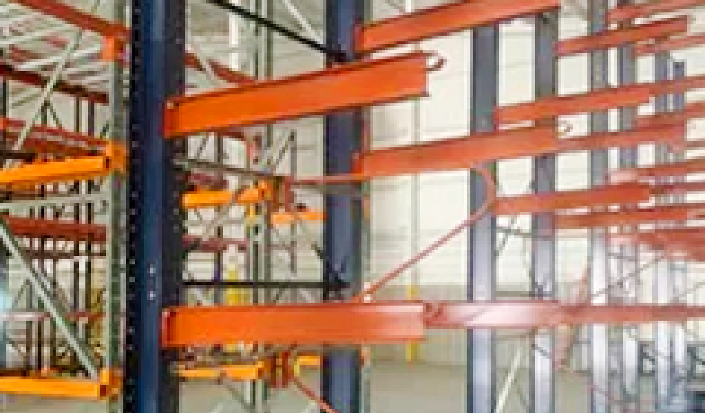 Empty industrial warehouse shelving units with metal frames and orange horizontal beams, including sturdy cantilever rack designs, are arranged in rows.