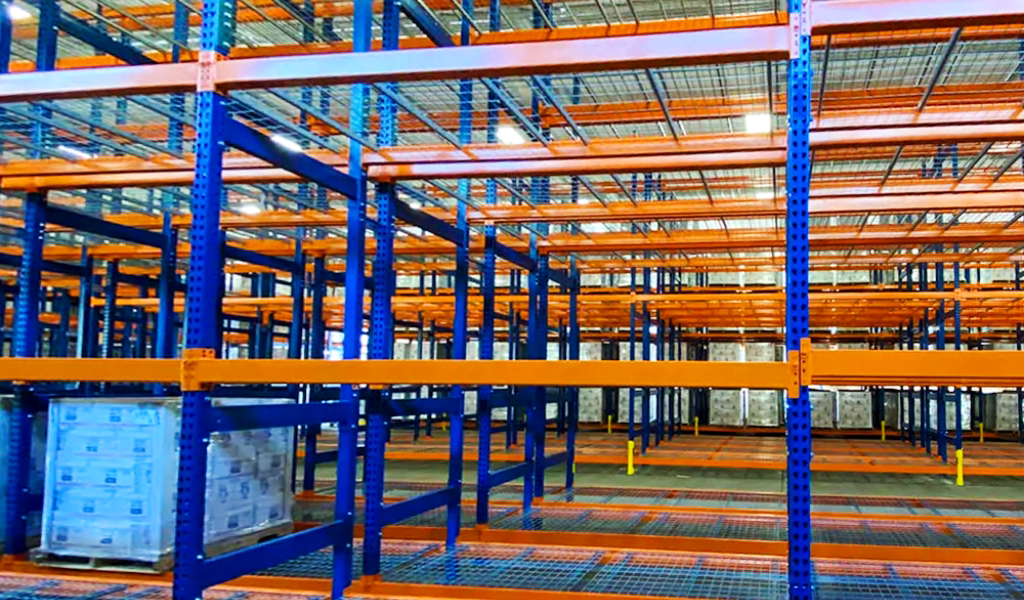 Empty industrial warehouse shelving units with blue frames and orange beams, except for a single pallet of goods on a lower shelf in the foreground, showcase a Double-Deep Rack system designed for efficient storage.