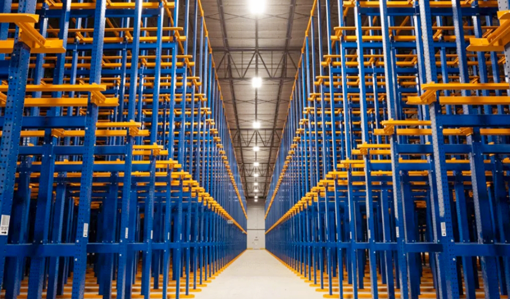 Empty blue and yellow Drive-In Rack shelving units are arranged in rows inside a brightly lit warehouse with a high ceiling.