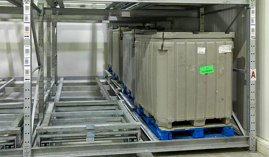 Large plastic containers are stored on blue pallets within a metal shelving rack system featuring push-back rack technology in an industrial warehouse.