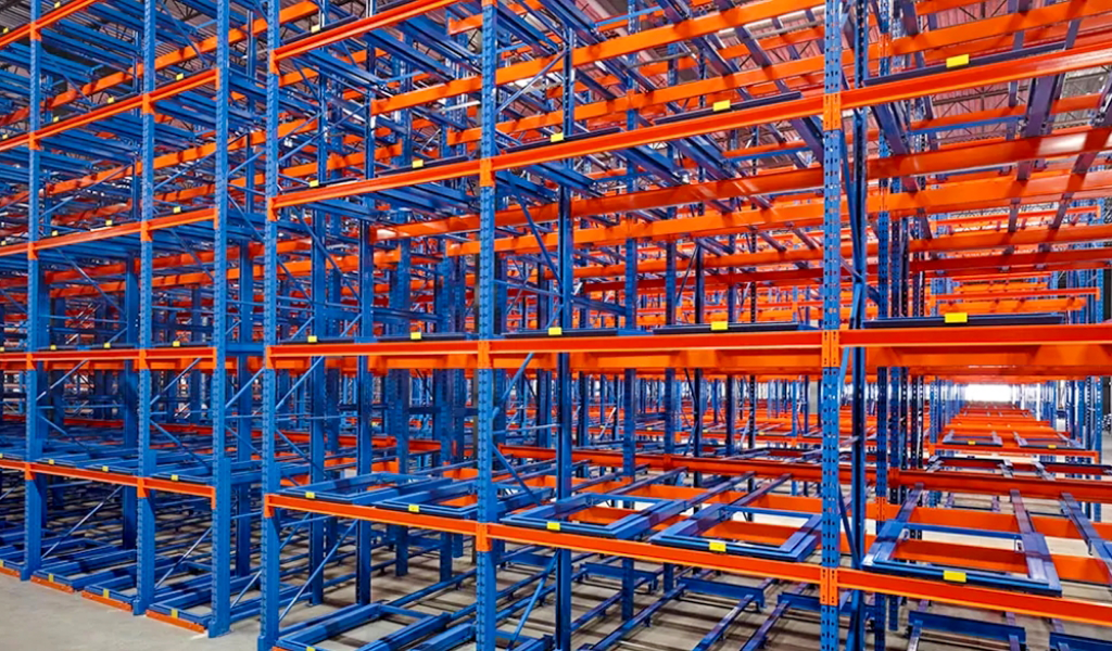 Rows of empty blue and orange industrial Push-Back Racks inside a warehouse form a grid-like metal framework, with no items stored on the shelves.