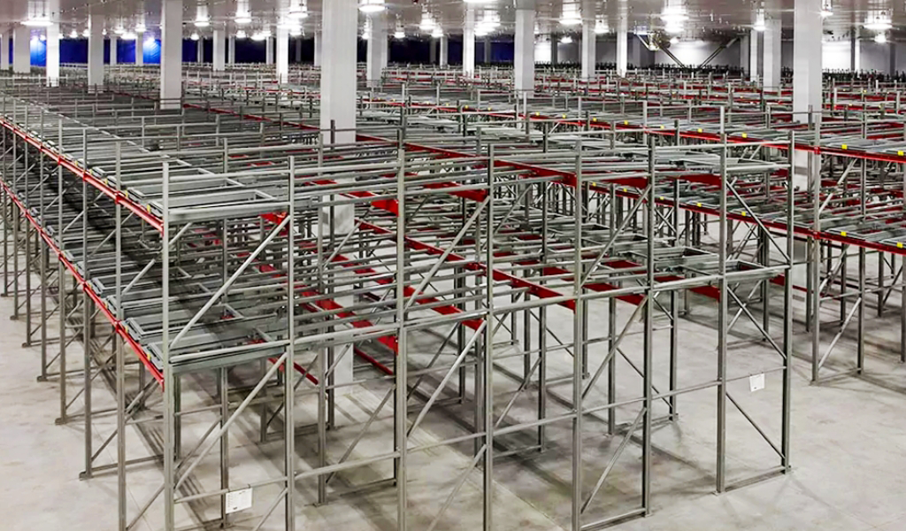 Large, empty warehouse interior with rows of metal shelving racks, including Push-Back Racks, and concrete floors, illuminated by overhead lighting.