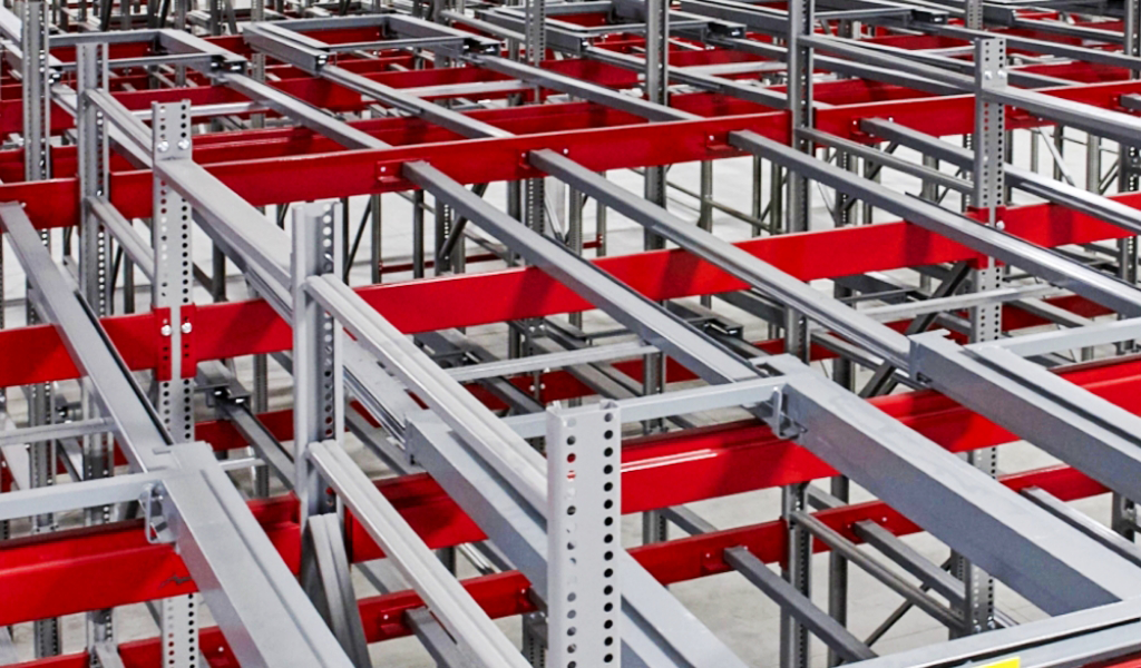Metal warehouse storage racks with red and gray steel beams are arranged in a grid pattern, featuring a Push-Back Rack system for efficient industrial storage solutions.