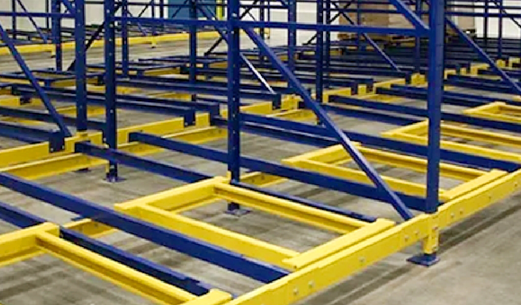 Blue and yellow industrial steel framework is installed on a concrete floor, forming the base structure for heavy-duty shelving or Push-Back Rack storage systems.