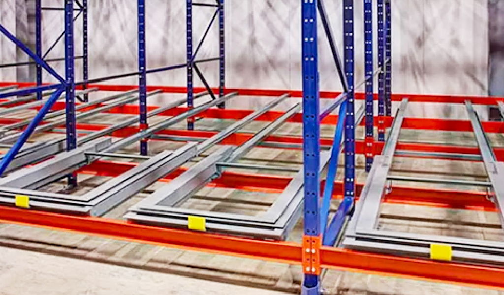 Push-Back Rack storage racks with blue and red frames stand on a concrete floor, featuring horizontal steel beams placed on the lower supports.