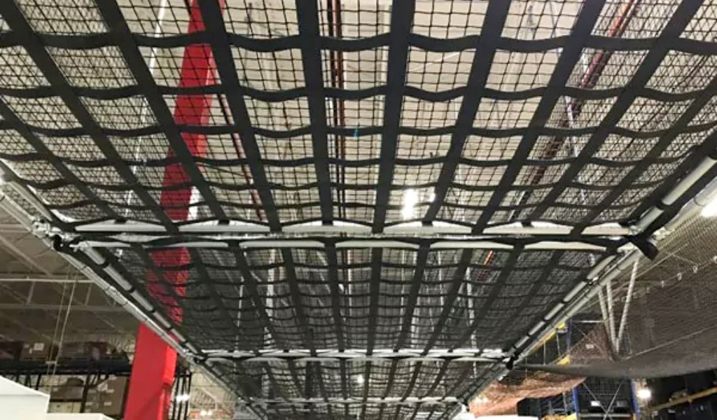 A close-up view of a Warehouse Safety Netting installation in an industrial warehouse, with visible steel beams and lighting above.