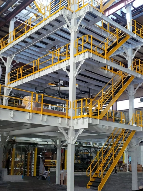 Three-level industrial Steel Platforms & Mezzanines structure with yellow railings and stairs inside a warehouse or factory setting.