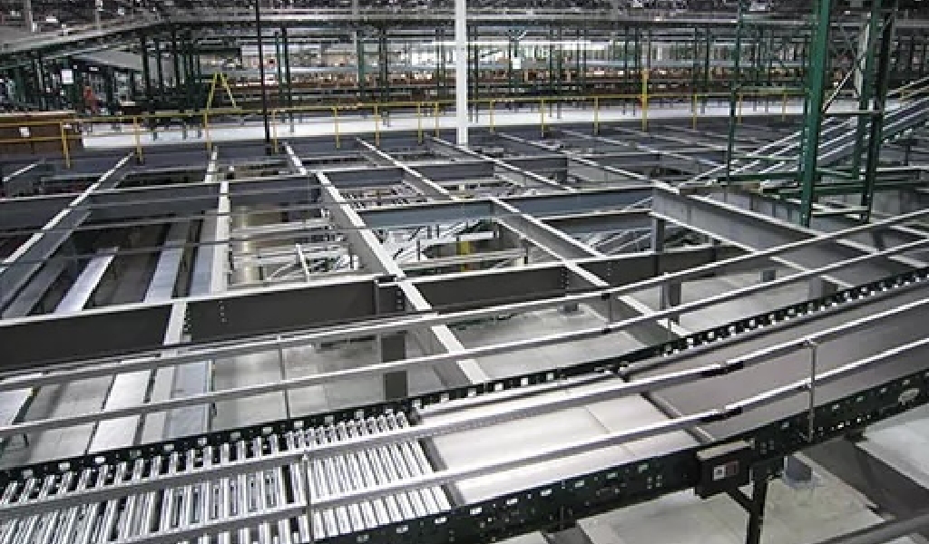 A large industrial facility with metal conveyor belts, steel framework, and Steel Platforms & Mezzanines under construction or installation, with overhead lighting and support structures visible.