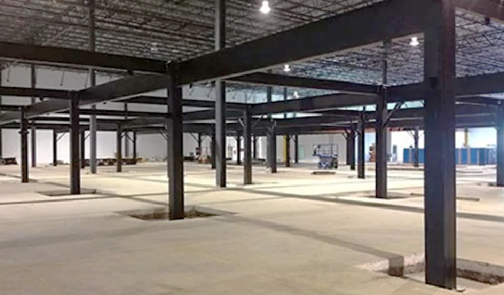 Large industrial warehouse interior featuring exposed steel beams, concrete floor, and Steel Platforms & Mezzanines visible among partial construction materials in the background.