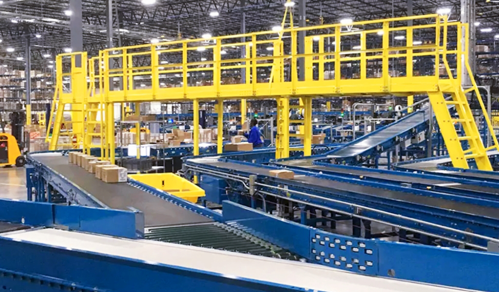 A large warehouse with blue conveyor belts, yellow elevated walkways, and sturdy steel platforms & mezzanines where packages are sorted and transported throughout the facility.